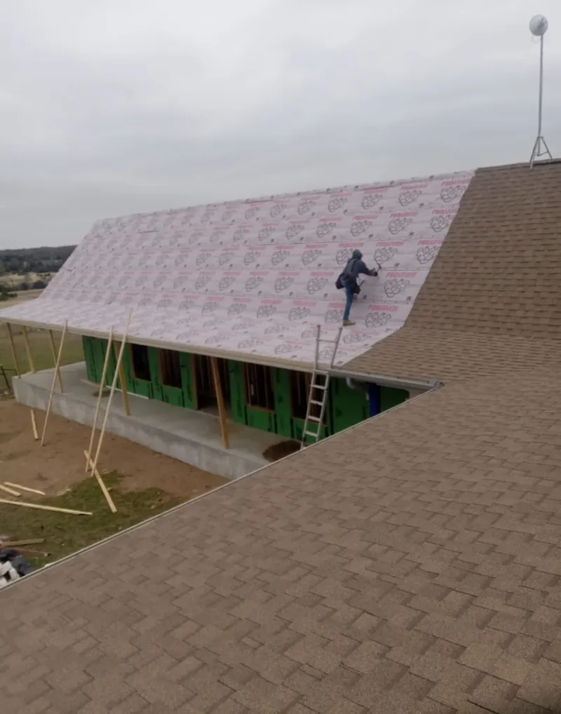 Worker preparing underlayment for a metal roof installation in Plum